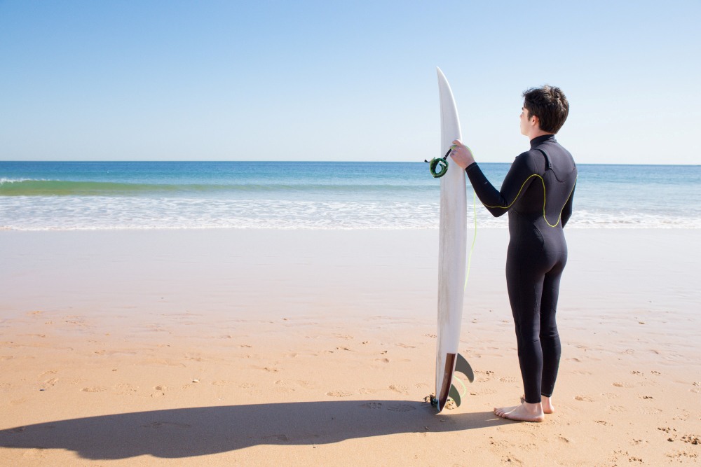 surfista en la playa junto a su tabla y con el neopreno